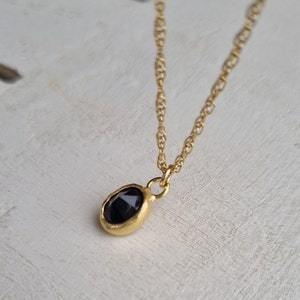May include: A gold chain necklace with a small, oval-shaped pendant featuring a black gemstone.