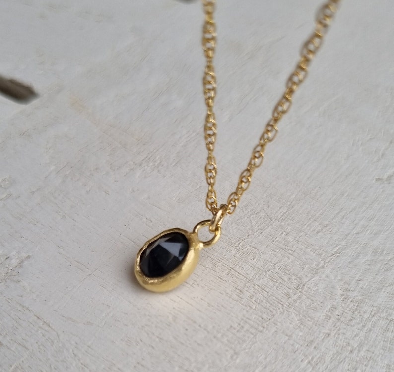 May include: A gold chain necklace with a small, oval-shaped pendant featuring a black gemstone.