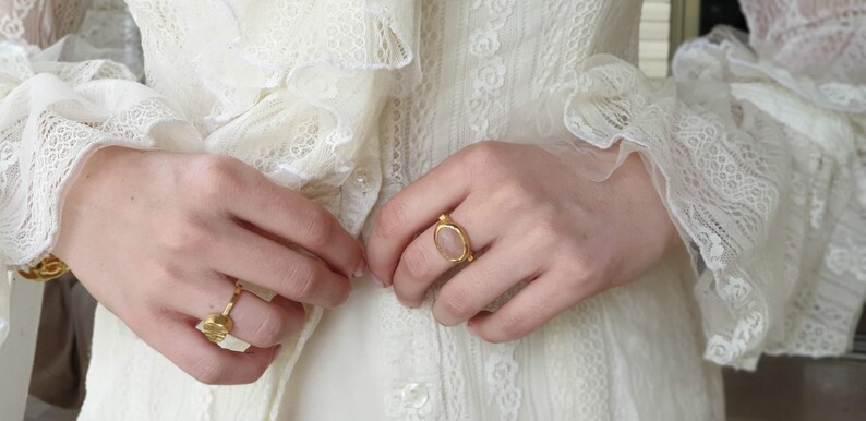 Puede incluir: Una mano de mujer con un anillo de oro con una piedra ovalada de color rosa claro. El anillo est&aacute; en el dedo medio de la mano. La mano lleva un vestido blanco de encaje.