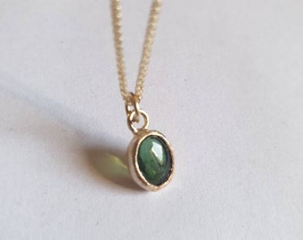 May include: A delicate gold chain necklace with a small oval pendant featuring a green gemstone.
