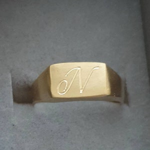May include: A gold signet ring with a square face and the letter "N" engraved on it.