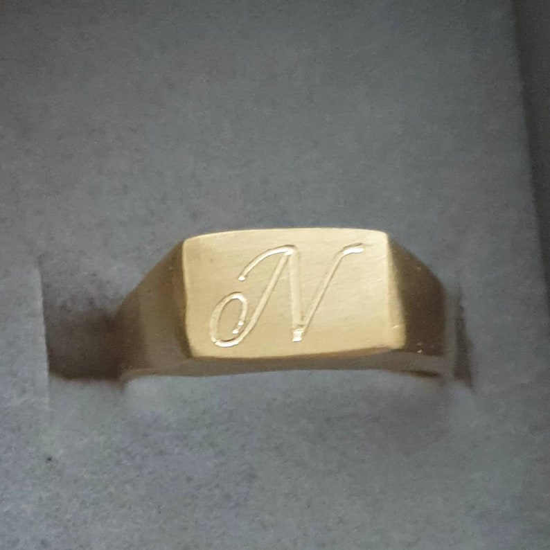 May include: A gold signet ring with a square face and the letter "N" engraved on it.