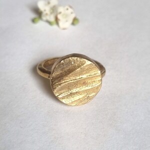May include: A gold ring with a textured, circular design. The ring is made of metal and has a simple, modern style.