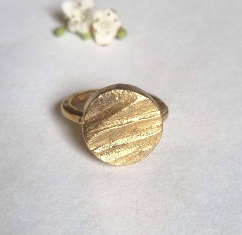 May include: A gold ring with a textured, circular design. The ring is made of metal and has a simple, modern style.
