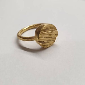 May include: A gold ring with a textured, round top. The ring is made of metal and has a simple design.