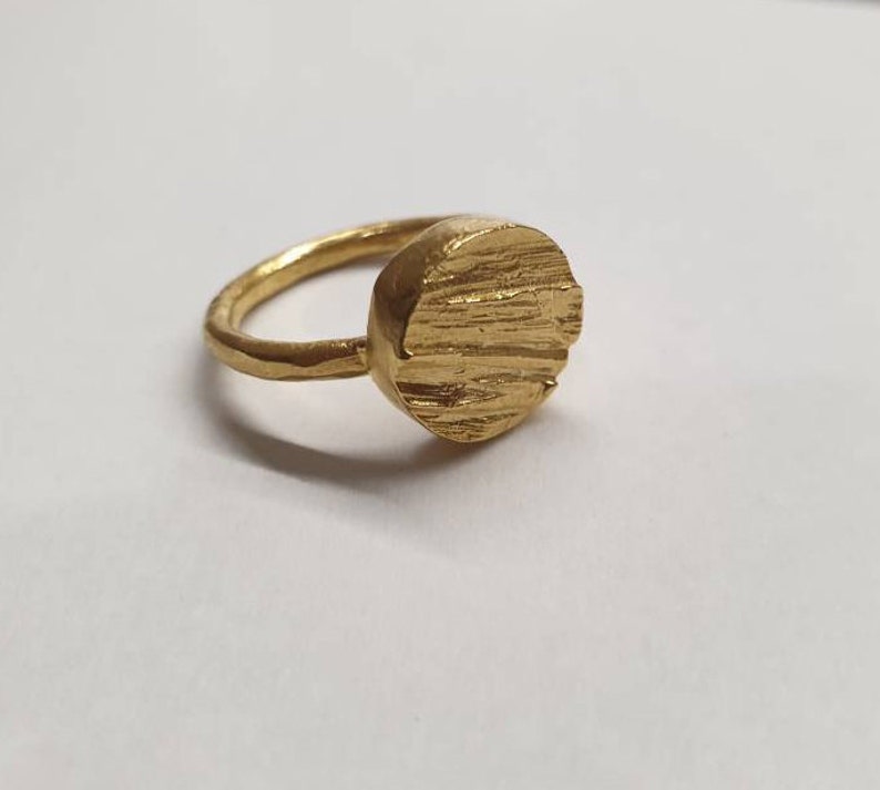 May include: A gold ring with a textured, round top. The ring is made of metal and has a simple design.