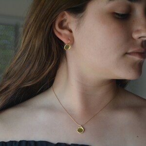 May include: A gold necklace with a small, round pendant. The pendant has a textured, hammered finish. The necklace is worn by a person with long brown hair.