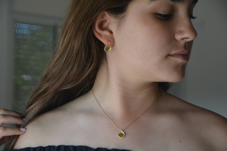 May include: A gold necklace with a small, round pendant. The pendant has a textured, hammered finish. The necklace is worn by a person with long brown hair.