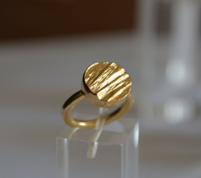 May include: A gold ring with a textured, round top. The ring is made of a smooth, shiny metal.