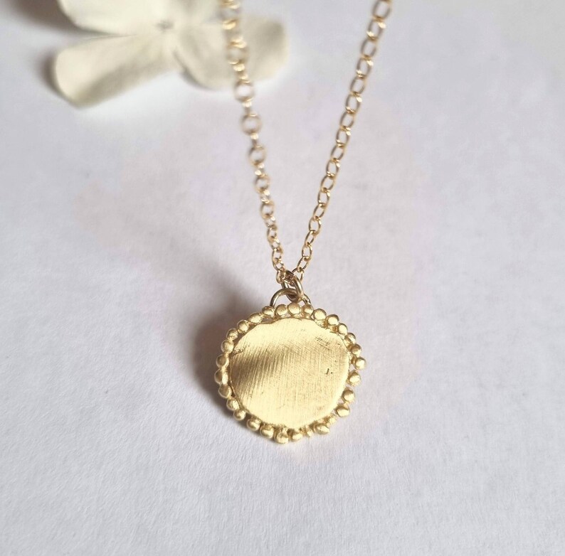 May include: A gold necklace with a round pendant. The pendant has a textured surface and a beaded edge.