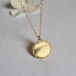 May include: A gold necklace with a round pendant. The pendant has a smooth, textured surface and a beaded edge.