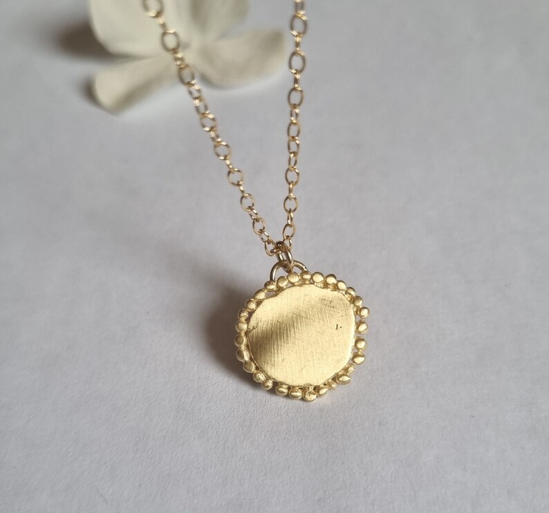 May include: A gold necklace with a round pendant. The pendant has a smooth, textured surface and a beaded edge.