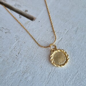 May include: A gold chain necklace with a round pendant. The pendant has a rope-like edge and a smooth, flat surface.
