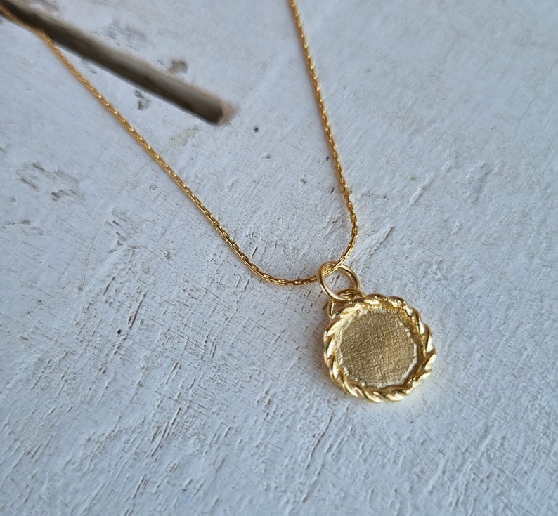 May include: A gold chain necklace with a round pendant. The pendant has a rope-like edge and a smooth, flat surface.