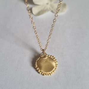 May include: A gold necklace with a round pendant. The pendant has a textured surface and a beaded edge.