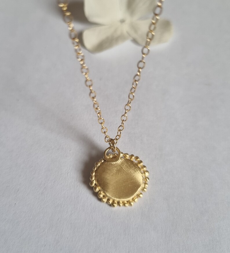 May include: A gold necklace with a round pendant. The pendant has a textured surface and a beaded edge.