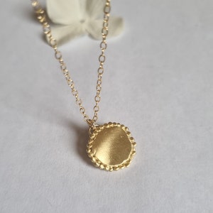 May include: A gold necklace with a round pendant. The pendant has a textured surface and a beaded edge.