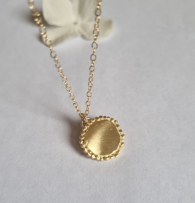 May include: A gold necklace with a round pendant. The pendant has a textured surface and a beaded edge.