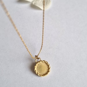 May include: A gold chain necklace with a round pendant. The pendant has a rope-like border.