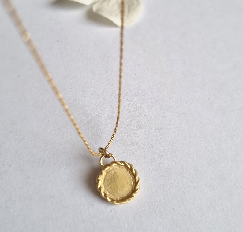 May include: A gold chain necklace with a round pendant. The pendant has a rope-like border.
