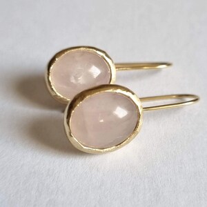 May include: A pair of gold earrings with pink rose quartz stones. The earrings have a simple, elegant design.