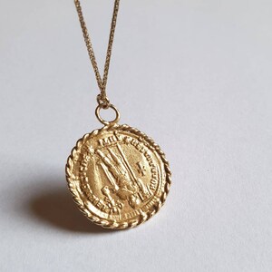May include: Gold pendant necklace with a round, detailed medallion featuring a religious figure. The medallion has a rope-like border and inscription.
