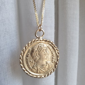 May include: A gold chain necklace with a round pendant featuring a profile of a person with a crown. The pendant has a rope-like border and the inscription "IMP. CAES. FL. ANN. VERUS. AUG. P. F. A." around the edge.