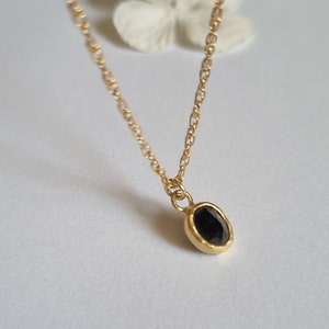May include: A delicate gold chain necklace with a small oval pendant featuring a black gemstone.