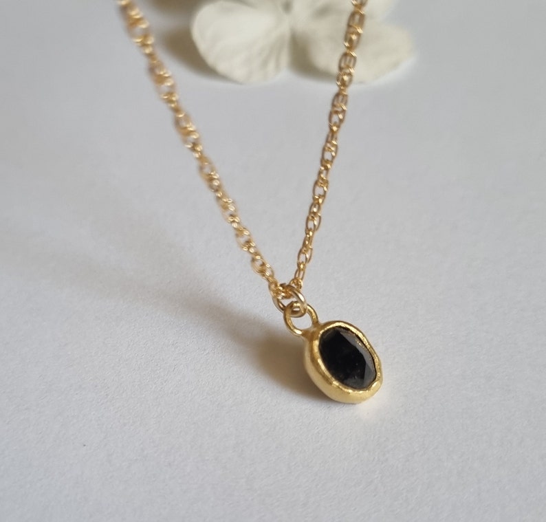 May include: A delicate gold chain necklace with a small oval pendant featuring a black gemstone.