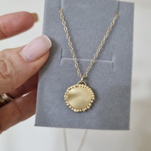 May include: A gold necklace with a round pendant. The pendant has a textured surface and is surrounded by small beads.