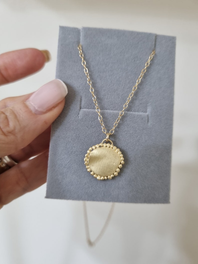 May include: A gold necklace with a round pendant. The pendant has a textured surface and is surrounded by small beads.