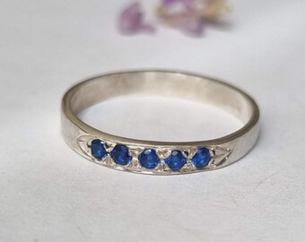 May include: A silver band ring with five blue sapphires set in a row.