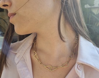 Puede incluir: Un collar de cadena de oro con eslabones triangulares. El collar lo lleva una persona con el pelo largo y castaño y una camisa rosa.