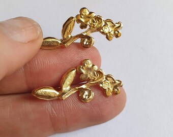 May include: Two gold-toned floral earrings with a delicate branch design. Each earring features a cluster of small flowers and leaves.