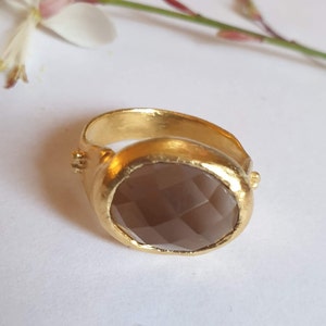 Puede incluir: Un anillo de oro con una piedra preciosa grande, ovalada y de color marr&oacute;n. El anillo tiene un acabado texturizado y martillado.