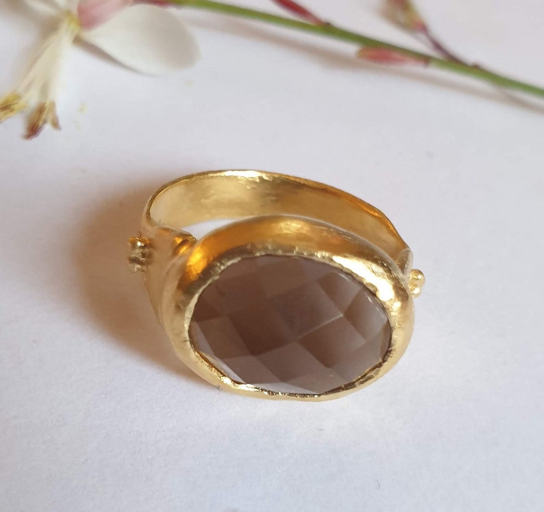 Puede incluir: Un anillo de oro con una piedra preciosa grande, ovalada y de color marr&oacute;n. El anillo tiene un acabado texturizado y martillado.