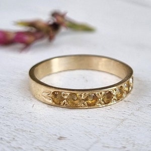 May include: A gold band ring with a row of small, round, yellow gemstones set in the band.