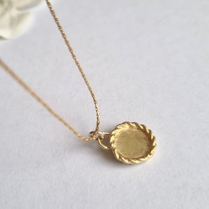 May include: A gold necklace with a round pendant featuring a rope-like border. The pendant is blank and ready for personalization.