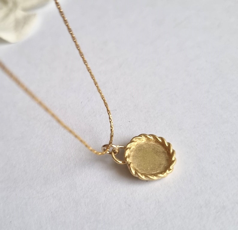 May include: A gold necklace with a round pendant featuring a rope-like border. The pendant is blank and ready for personalization.