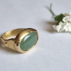 Puede incluir: Un anillo de oro con una piedra ovalada verde engastada en una banda texturizada.