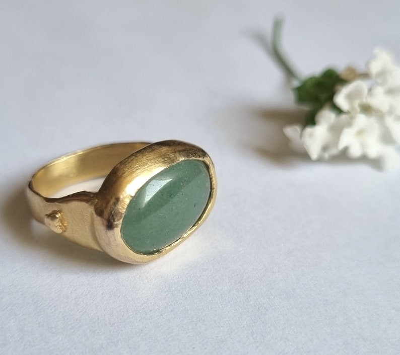 Puede incluir: Un anillo de oro con una piedra ovalada verde engastada en una banda texturizada.