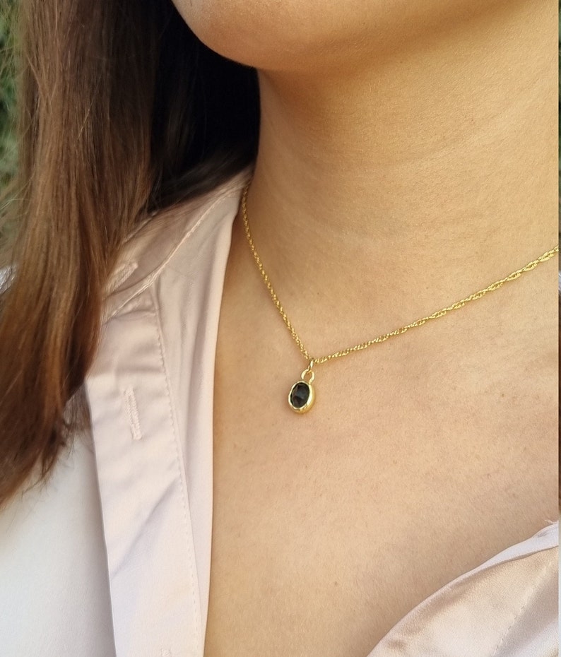 May include: A gold chain necklace with a small, round, black gemstone pendant.