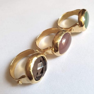 Puede incluir: Tres anillos de oro con piedras preciosas de diferentes colores. Los anillos tienen un acabado texturizado y martillado. Las piedras preciosas son verde claro, rosa claro y marr&oacute;n oscuro.