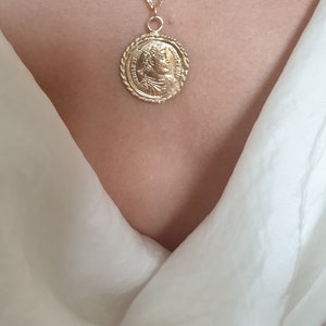 May include: A gold chain necklace with a large oval pendant featuring a detailed profile of a person. The pendant has a rope-like border.