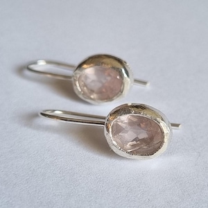 May include: A pair of silver earrings with a light pink oval-shaped gemstone set in each earring.