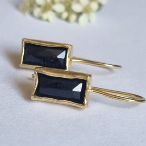 Pode incluir: Um par de brincos de ouro com pedras retangulares pretas. Os brincos têm um design simples e minimalista.