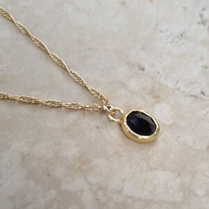 May include: A gold chain necklace with a black oval pendant. The pendant has a textured gold frame.