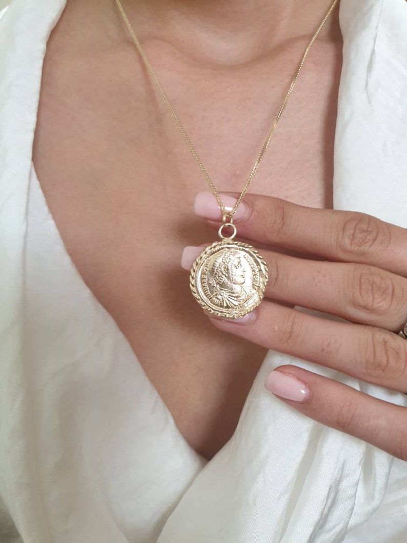 May include: A gold chain necklace with a large, round pendant featuring a detailed profile of a person. The pendant has a rope-like border.
