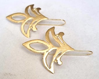 May include: A pair of gold-toned earrings with a delicate, floral design. The earrings are made of metal and have a hook closure.