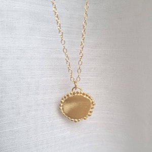 May include: A gold necklace with a round pendant that has a textured surface and a beaded edge.